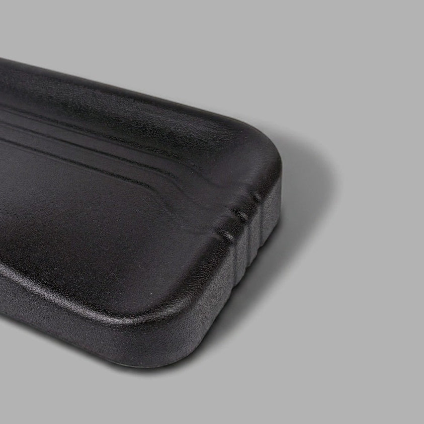 A black molded plastic seat cushion or support pad with a textured surface and curved contours, shown on a plain gray background.