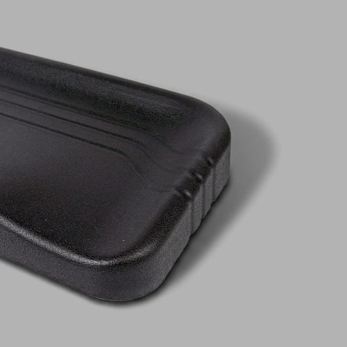 A black molded plastic seat cushion or support pad with a textured surface and curved contours, shown on a plain gray background.
